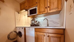 A compact kitchen with wooden cabinets, a microwave, a sink, and a washing machine. - 300m from resort center, 1st floor, balcony, tv, 33m², Serre Chevalier (Le Monêtier-les-Bains)