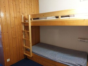 A bunk bed with a wooden ladder, a mattress with a polka dot cover, and a wall-mounted air vent.