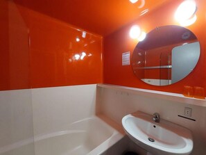 A bathroom with a white bathtub, a sink, and a mirror with lights above.
