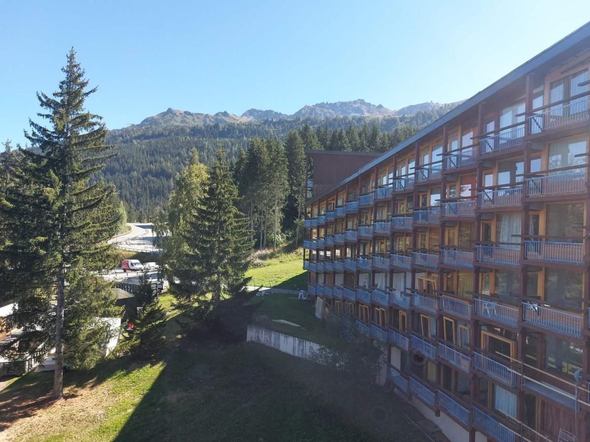 A multi-story hotel with balconies, surrounded by trees and mountains.