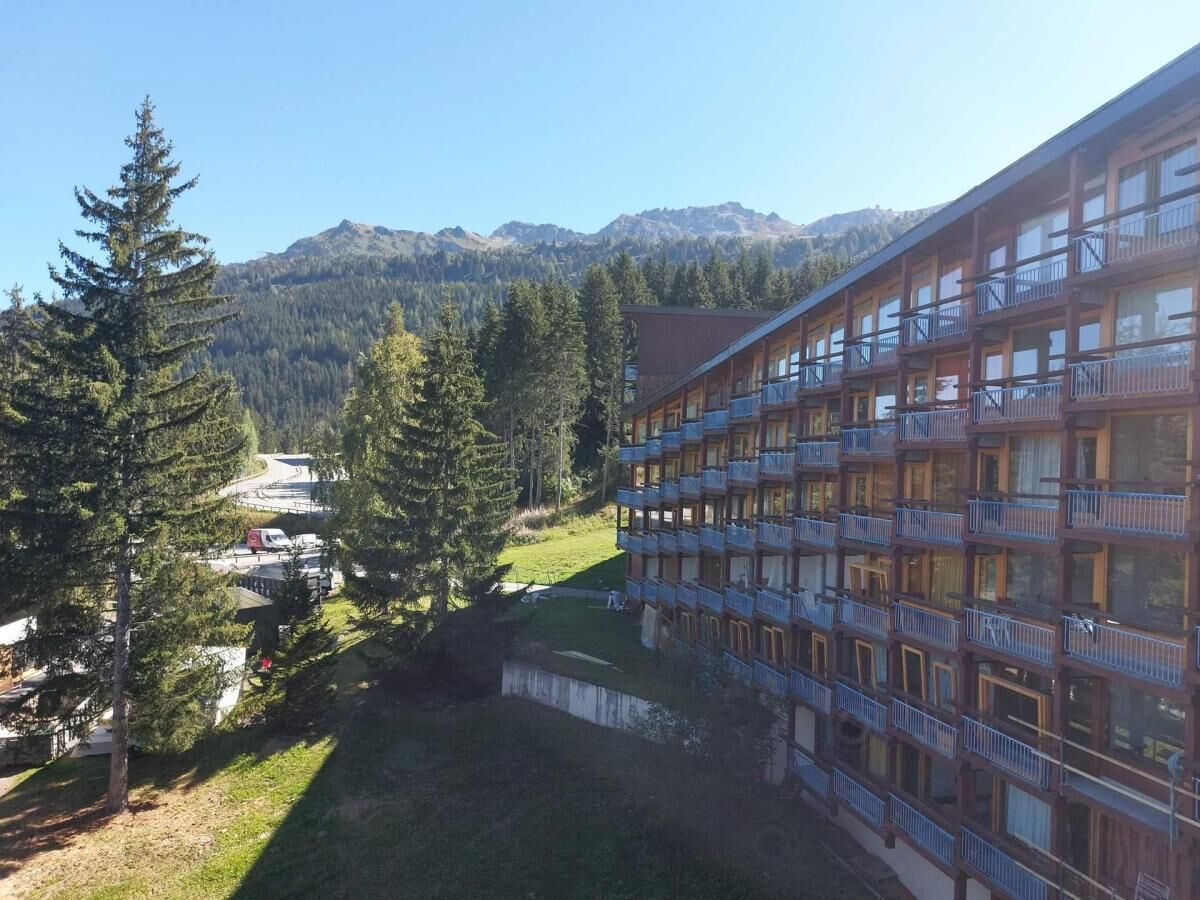 A multi-story hotel with balconies, surrounded by trees and mountains.