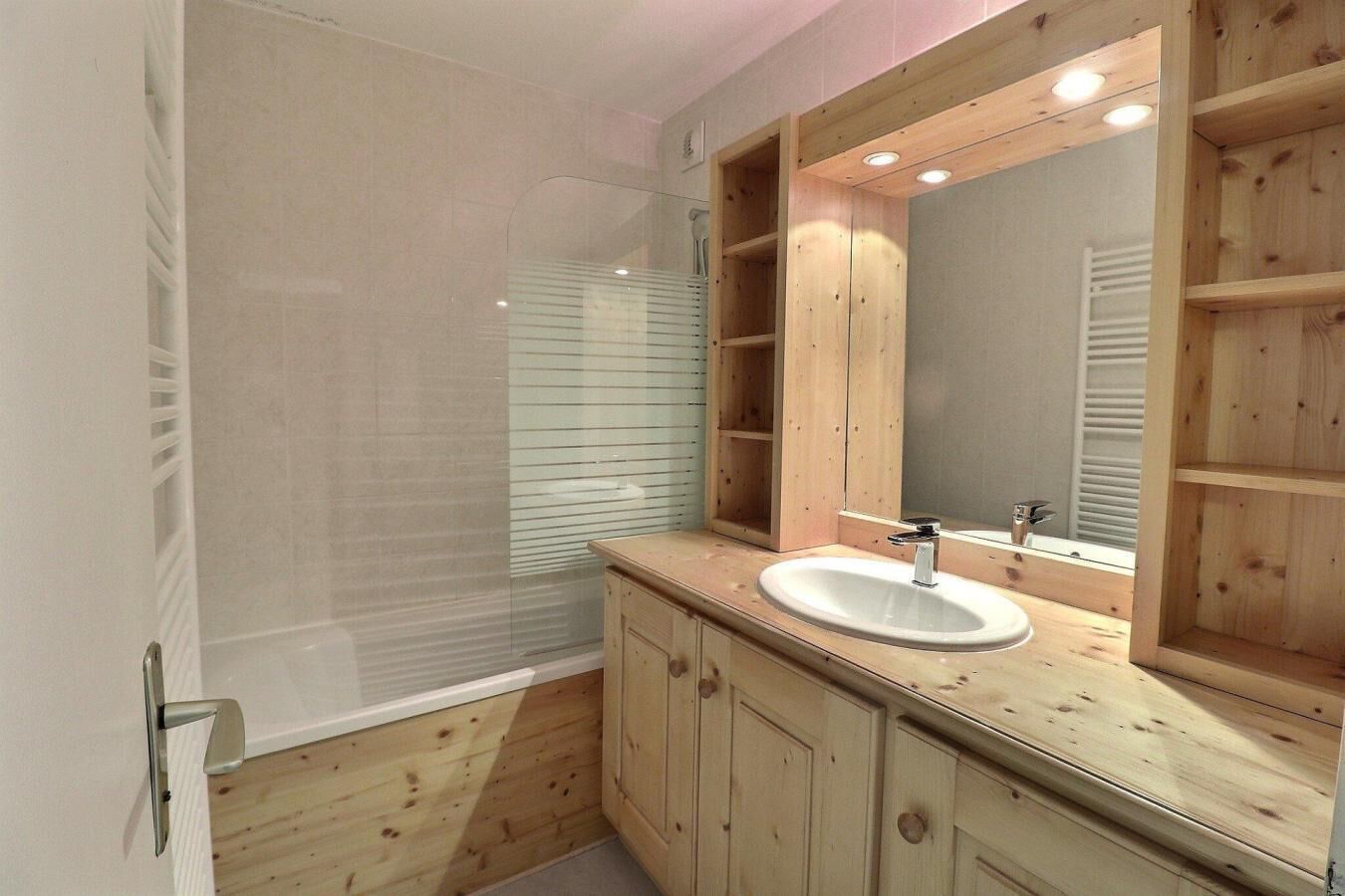 Un bagno moderno con box doccia in vetro, mobile bagno in legno e uno specchio grande.