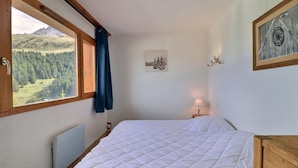A bedroom with a large window, a bed, a bedside table, and a wall-mounted lamp. - 10m from ski slopes, 1st floor, balcony, 33m², Méribel-Mottaret (Méribel - Les Allues)