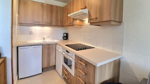 A compact kitchen with wooden cabinets, a built-in dishwasher, a stove, and a coffee maker. - 10m from ski slopes, 1st floor, balcony, 33m², Méribel-Mottaret (Méribel - Les Allues)