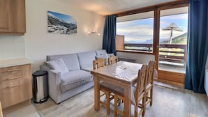 A cozy room with a sofa, a dining table, and a view of a mountainous landscape through a large window. - 10m from ski slopes, 1st floor, balcony, 33m², Méribel-Mottaret (Méribel - Les Allues)