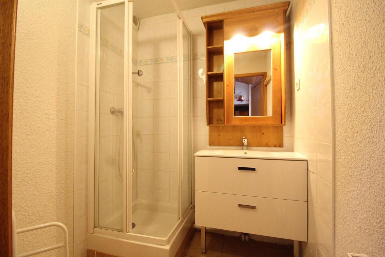 Un bany amb dutxa tancada amb vidre, un tocador de fusta amb mirall i un lavabo blanc.