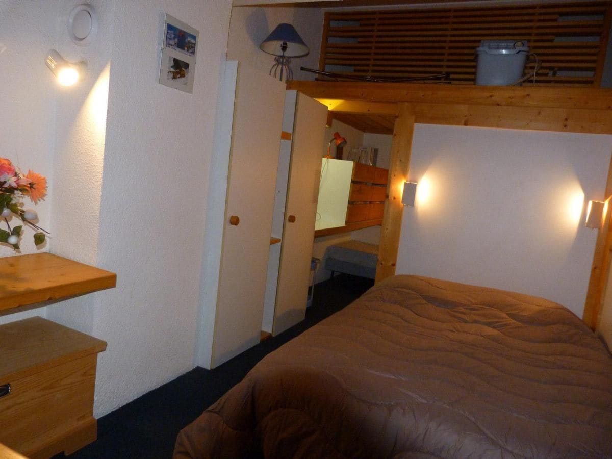 Een kleine kamer met een bed, een houten bureau en een klein plankje.