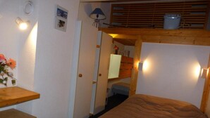 Een kleine kamer met een bed, een houten bureau en een klein plankje.