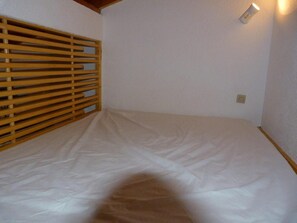 Een kamer met een bed, een houten lattenpannen hoofdbord, een wandlamp en een stopcontact.