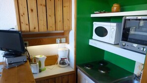 Een kleine keuken met houten kastjes, een magnetron, een fornuis en een koffiezetapparaat.