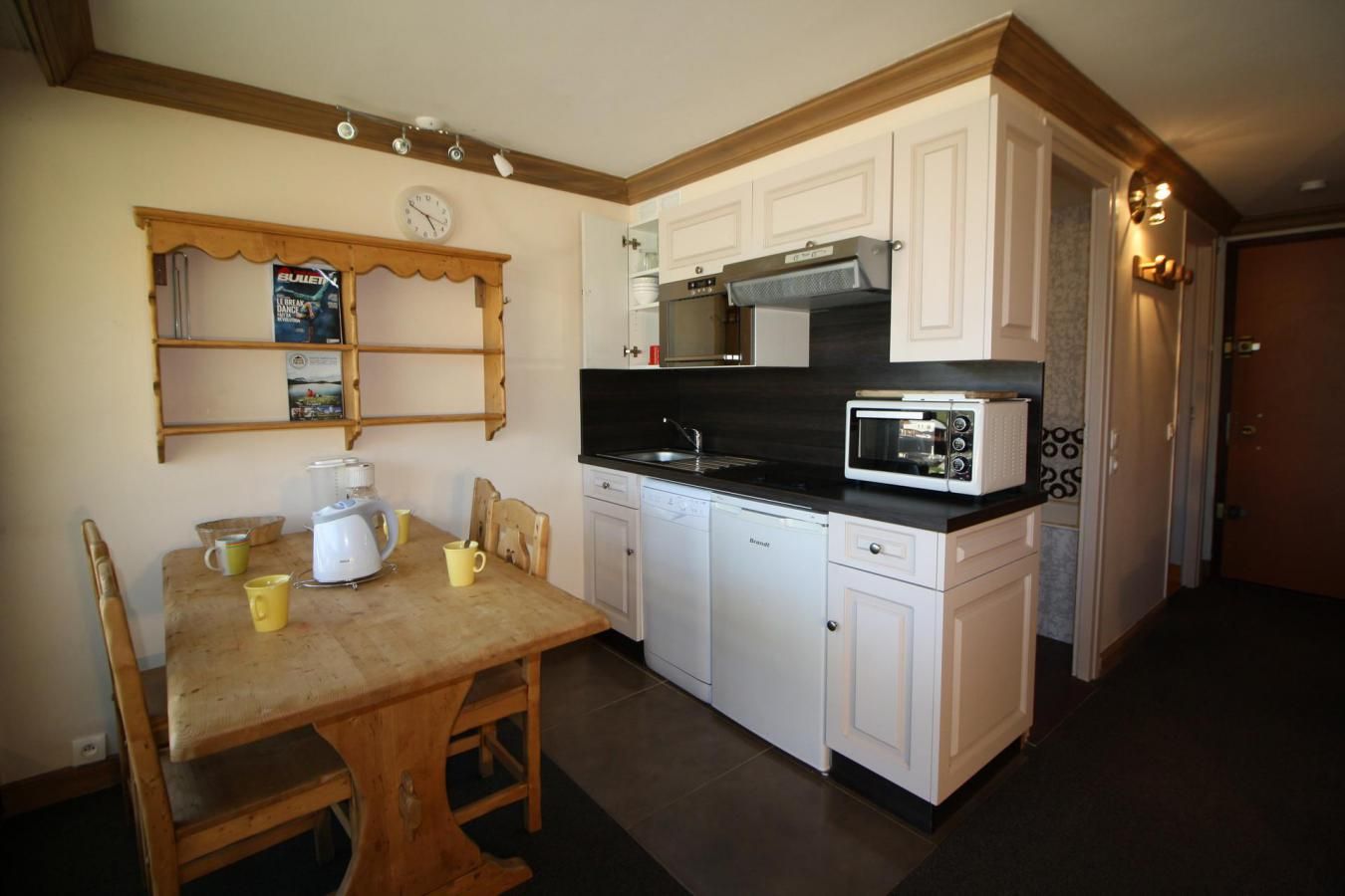 A compact kitchen with white cabinets, a microwave, a sink, and a wooden dining table with chairs.