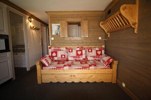 A cozy wooden sofa with a checkered cushion in a room with wooden walls and a small window.