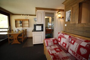 A compact living space with a kitchenette, a dining area, and a sofa with a patterned cover.