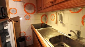 Eine Küche mit Spüle aus Edelstahl, Holzschränken und dekorativen, orange-weißen Fliesen.