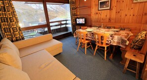 Ein gemütliches Zimmer mit einer Couch, einem Holzesstisch, Stühlen und einem Fernseher.