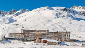 Un hôtel à plusieurs étages, avec des pistes de ski en arrière-plan et un paysage montagneux.