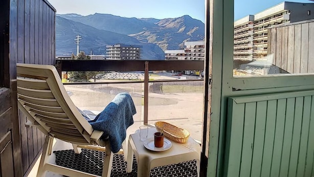 A balcony with a chair, a table with a basket and a cup, and a view of mountains and buildings. - Ski-in/ski-out & foot of the slopes, 1st floor, balcony, tv, 22m², Les Menuires (Les Menuires)