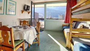 A room with a bunk bed, a dining table with chairs, a television, and a window with a view of mountains and buildings. - Ski-in/ski-out & foot of the slopes, 1st floor, balcony, tv, 22m², Les Menuires (Les Menuires)