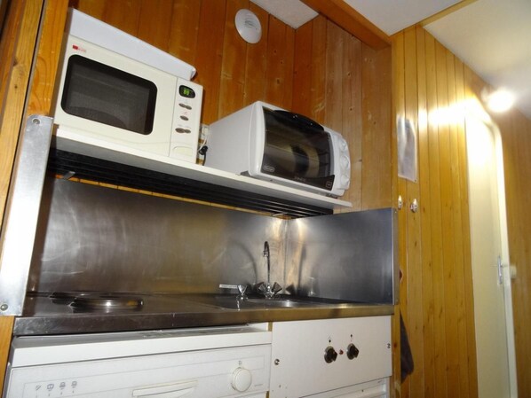 A compact kitchen with a microwave, toaster, and stainless steel sink.