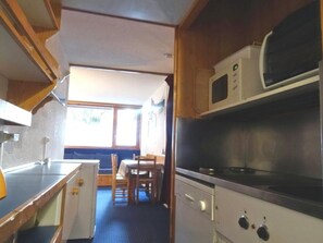 A compact kitchen with a microwave, stove, and small refrigerator. There is a dining area with a table and chairs.