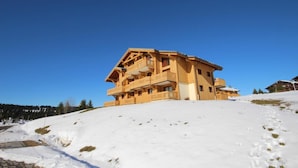 Un chalé de madera de varios pisos con balcones, ubicado en una ladera cubierta de nieve.