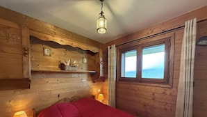 Una habitación de cabaña de madera con una cama, un ventanal y un estante con objetos.