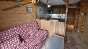 Un interior de cabaña acogedor con un sofá rojo a cuadros, paredes de madera, una zona de cocina y una pared de piedra.