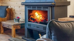 A wood-burning stove with a fire burning inside, placed in a room with wooden walls and furniture. - Chalet, 350m from ski lifts, sauna, terrace, fireplace or stove, parking, tv, 100m² (Peisey-Nancroix)