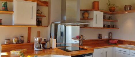 A kitchen with white cabinets, a stainless steel range hood, wooden countertops, and various kitchen appliances.
