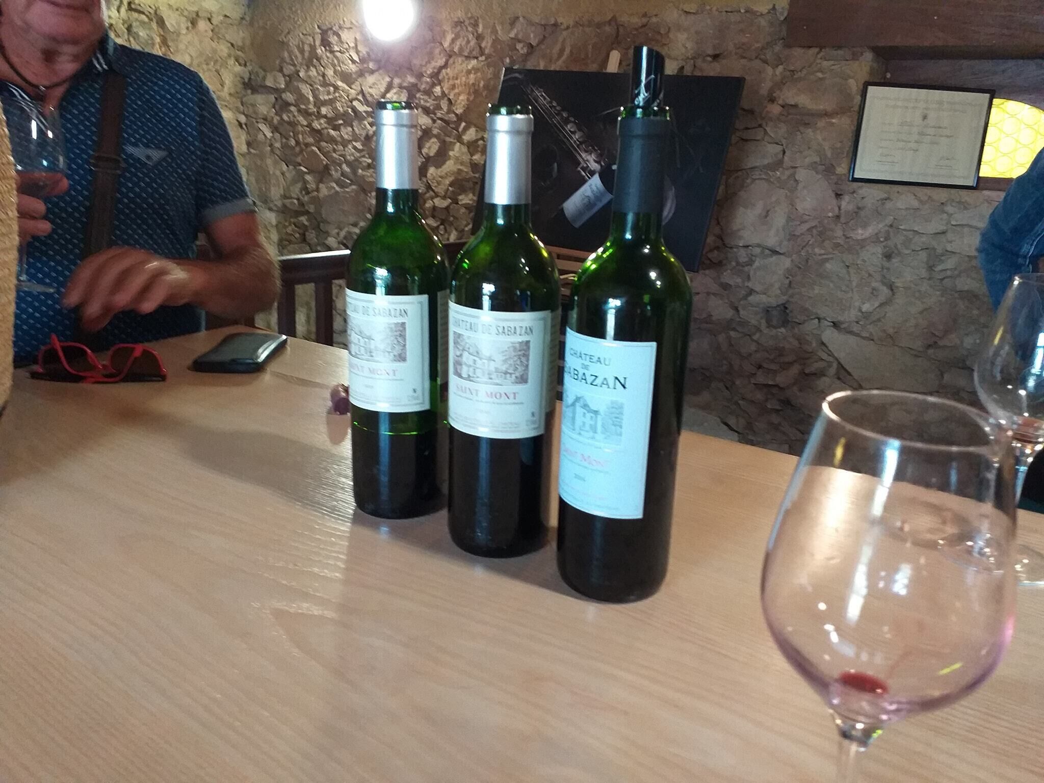 Three wine bottles on a wooden table with a stone wall background.