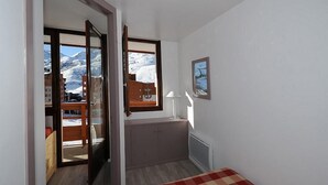 A room with a bed, a window with a view of mountains, a lamp, and a painting on the wall. - 3rd floor, view ski slopes/mountain/ski slopes, balcony, tv, ski locker, 25m², Les Menuires (Les Menuires)