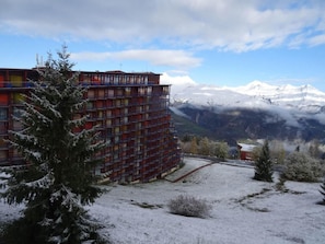 Um edifício com vários andares e varandas, rodeado por terreno coberto de neve e montanhas ao fundo.