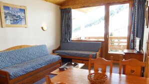 A cozy room with a sofa, a table, and chairs. There's a window with curtains, a wall-mounted light, and a framed picture. - 10m from ski slopes, 4th floor, balcony, 40m², Méribel-Mottaret (Méribel - Les Allues)