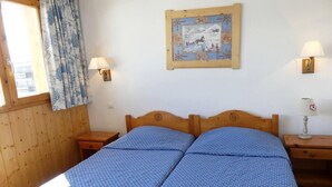 A double bed with a blue patterned bedspread, two bedside tables, a wall-mounted lamp, a window with curtains, and a framed picture on the wall. - 10m from ski slopes, 4th floor, balcony, 40m², Méribel-Mottaret (Méribel - Les Allues)