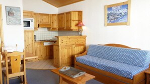 A cozy living room with a blue sofa, wooden furniture, a kitchen with wooden cabinets, and a framed picture on the wall. - 10m from ski slopes, 4th floor, balcony, 40m², Méribel-Mottaret (Méribel - Les Allues)