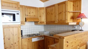 A compact kitchen with wooden cabinets, a microwave, a stove, and a sink. - 10m from ski slopes, 4th floor, balcony, 40m², Méribel-Mottaret (Méribel - Les Allues)