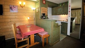 Una cocina acogedora con paredes de madera, una mesa de comedor con mantel a cuadros rojo y blanco, y una cafetera.