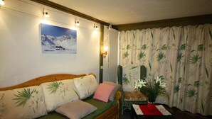 Una habitación acogedora con un sofá de madera, una mesita con un florero y un ventanal con cortinas.