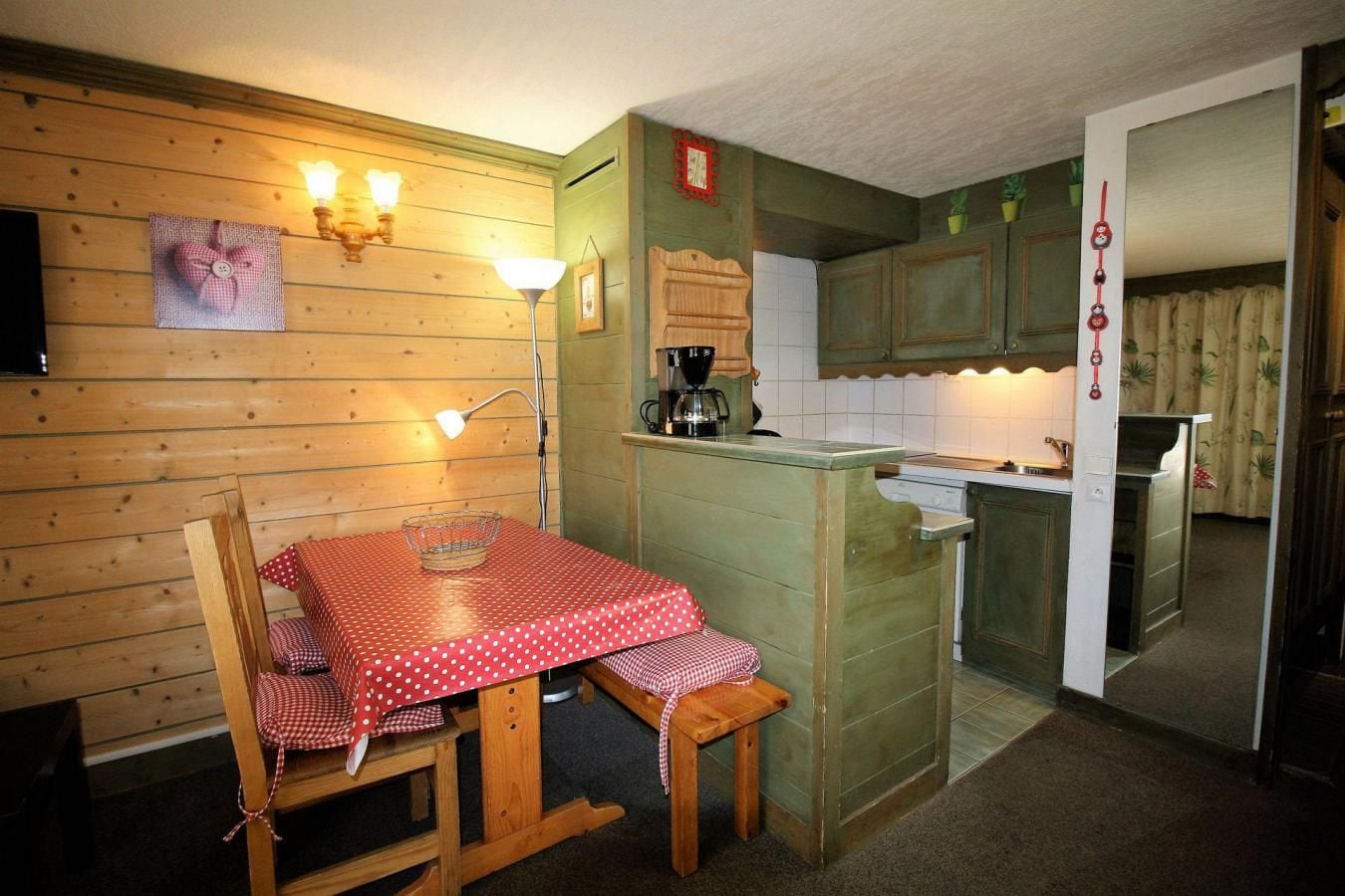 A cozy kitchen with wooden walls, a dining table with a red and white checkered tablecloth, and a coffee machine.