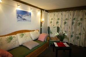 A cozy room with a wooden sofa, a small table with a vase, and a large window with curtains. - 10m from ski slopes, 2nd floor, view lake, terrace, tv, ski locker, 28m², Tignes (Tignes)