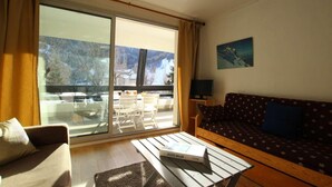 A living room with a sofa, a coffee table with a book, a TV, and a large window with a view of a snowy landscape. - 350m from ski slopes, 1st floor, terrace, parking, tv, 56m², Serre Chevalier (SERRE CHEVALIER)