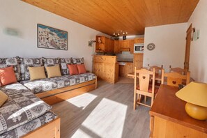 A cozy living area with a sofa, wooden dining table, and kitchen in the background.