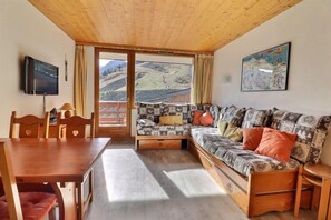 A cozy room with a wooden ceiling, a sofa with patterned cushions, a television, and a dining table with chairs.
