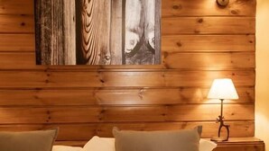 A wooden-paneled room with a bed, two pillows, a wall-mounted lamp, and a framed picture.