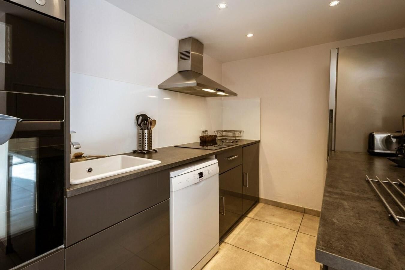 A modern kitchen with a stainless steel range hood, a dishwasher, and a countertop with kitchen utensils.