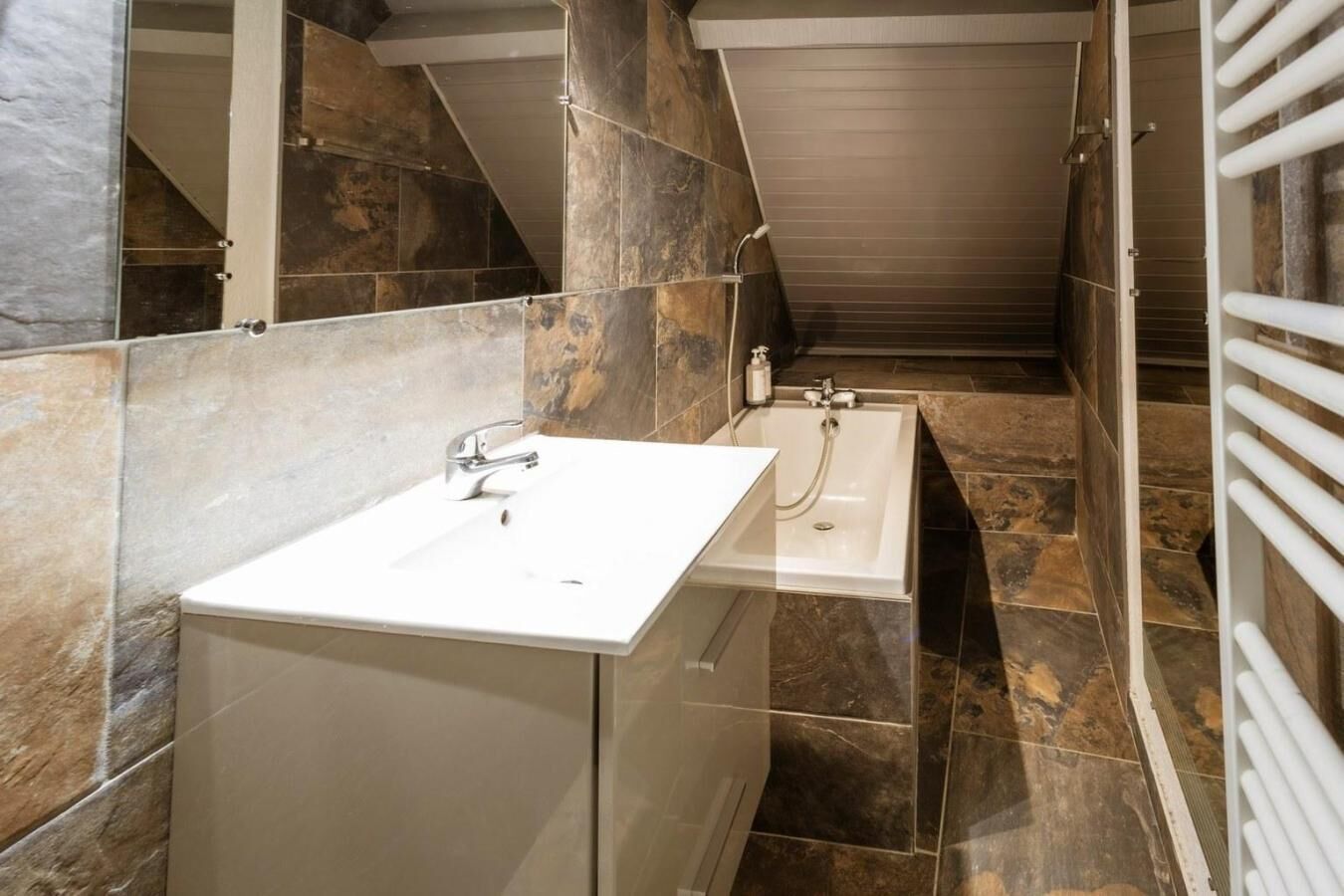 Un bagno moderno con un lavandino bianco, una vasca da bagno e una doccia. Le pareti sono rivestite con un mix di piastrelle con motivi in pietra e marmo.