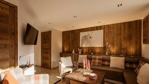 A cozy living room with a wooden wall, a flat-screen TV, a sofa, a coffee table, and a fireplace.