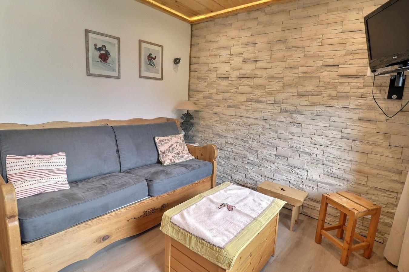A cozy room with a grey sofa, a small wooden table, and a TV mounted on the wall.