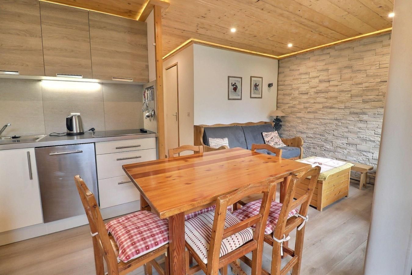 A compact kitchen with modern appliances, a wooden dining table with chairs, and a stone accent wall.