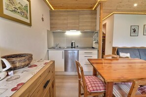 Cocina compacta con comedor, armarios de madera, pileta de acero inoxidable y una mesa con sillas.